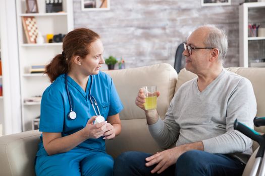 Senior man and lady nurse having a conversation in a nursing home. Elderly age man taking his pills.