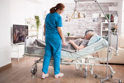 Old woman in nursing home smiling at female caretaker. Old woman laying on bed.