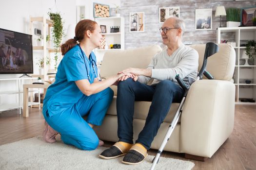 Old man with glasses sitting on couch in nursing room holding female doctor hand.