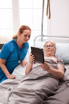 Elderly age woman and female doctor reading on tablet computer. Old woman in nursing home.