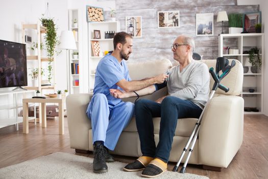 Caucasian young doctor in nursing home checking blood pressure of elderly age male with crutches.