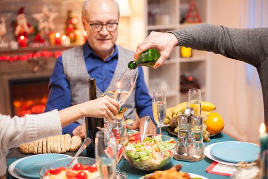 Shot of man pouring wine in a glass at christmas family dinner.