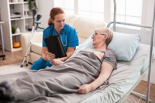 Female doctor in nursing home using tablet computer to show old woman medical results.