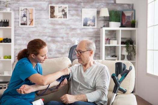 Female nurse attaching digital device on old mans arm to check blood pressure.