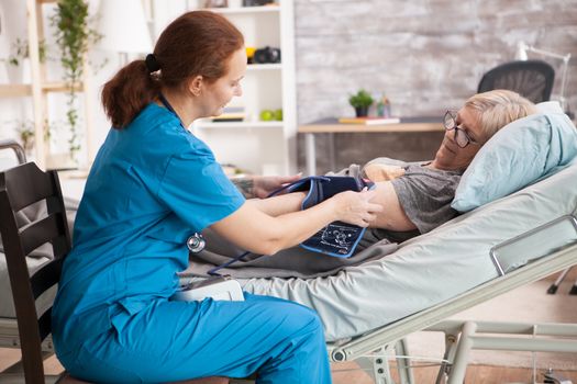 Female nurse in nursing home doing blood pressure measurement of a senior woman patient using digital device.