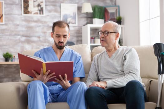 Male doctor reading a book for elderly age male in nursing home.