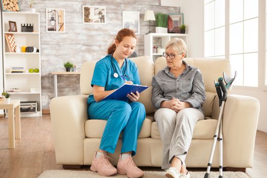 Female nurse writing on clipboard while talking with senior woman in nursing home.