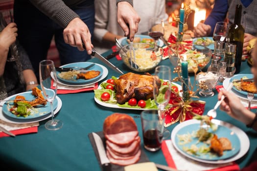 Close up of man slicing roasted chicken at christmas celebration for his family.