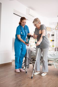 Female nursing old woman with rehabilitation in nursing home using crutches.