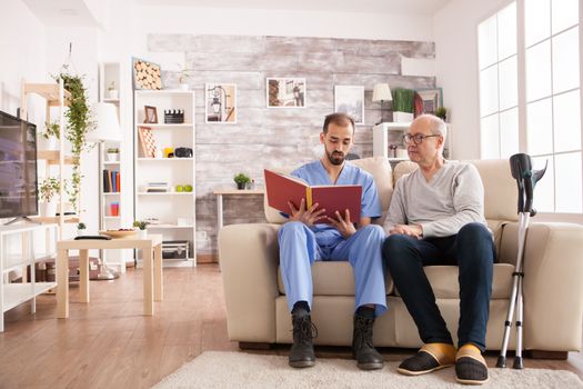 Male doctor in nursing home reading a book to old man with alzheimer.