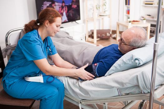 Female nurse checking the blood pressure of retired man in nursing home.