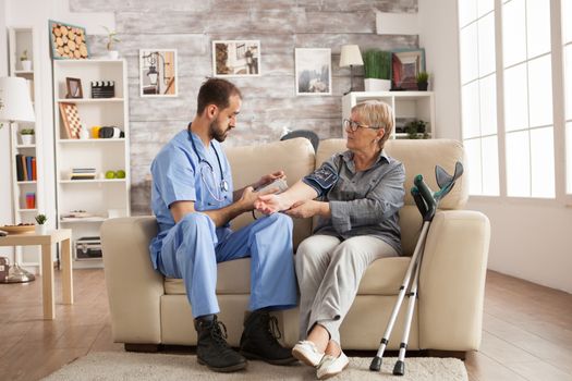 Male doctor with stethoscope around his neck taking the blood pressure of senior woman in nursing home.