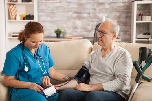 Female doctor in nursing home checking old man blood pressure.