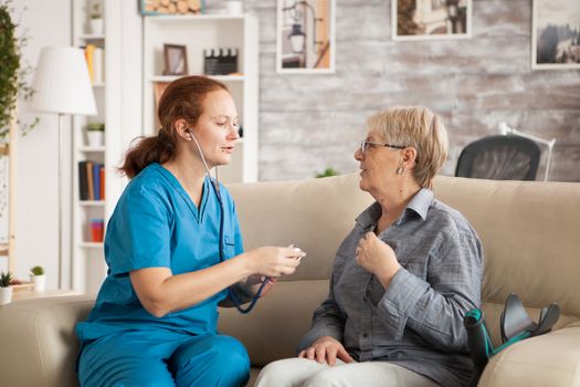 Female doctor in nursing home using stethoscope to listen old woman heart.