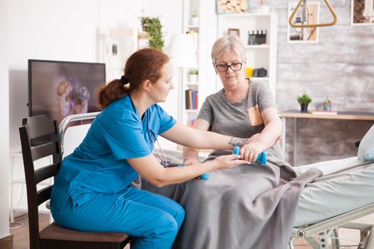 Senior woman training with physiotherapist in nursing home using dumbbells.