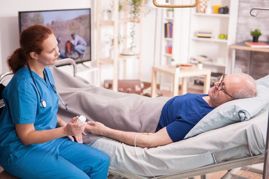 Elderly man in nursing home lying in bed talking with female doctor.