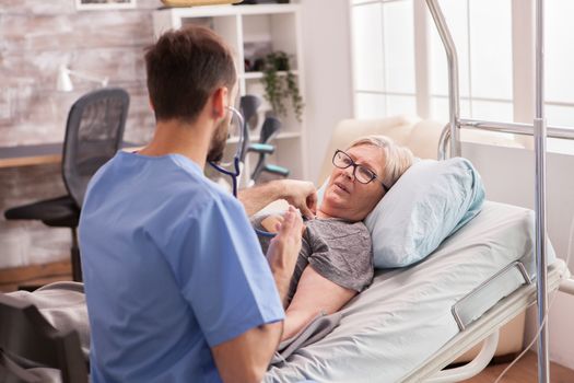 Back view of male doctor using stethoscope to check woman heart in nursing home.