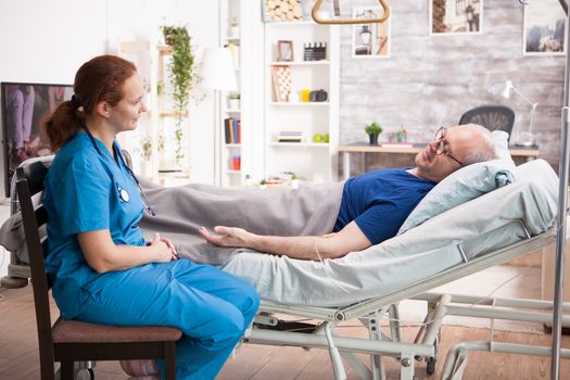 Photo of elderly age man laying on bed in nursing home holding the hand of female nurse.