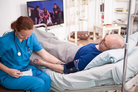 Female doctor reading blood pressure of old man on digital device in nursing home.