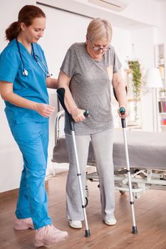 Female doctor helping old woman with crutches in nursing home.