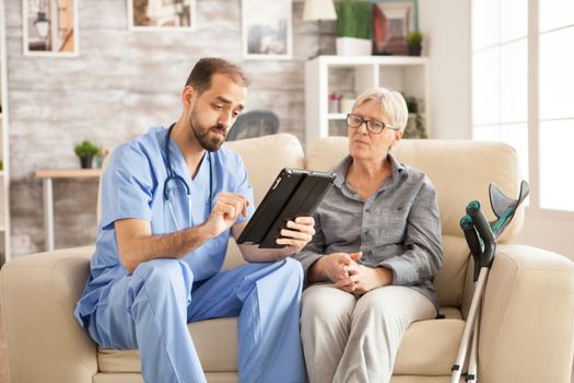 Doctor in nursing home using tablet computer while taking with female pensioner.