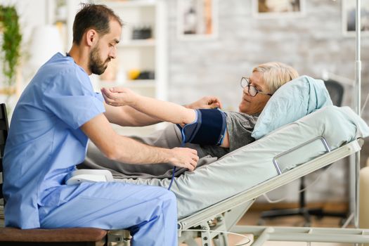 Young male doctor taking the blood pressure of senior woman in nursing home