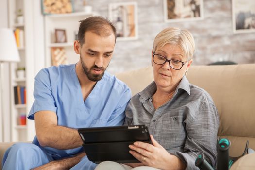 Male doctor helping caucasian senior woman to use her tablet computer in nursing home.