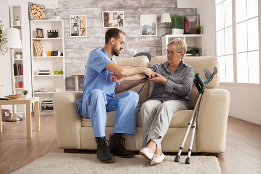 Male nurse using digital blood pressure device on senior woman in nursing home.