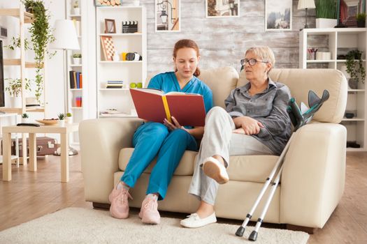 Nurse woman reading a book on nursing home for ill senior woman.