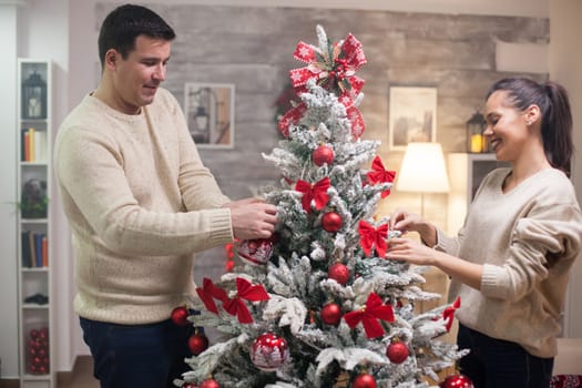 Young woman smiling while assembling christmas tree together with her husband.