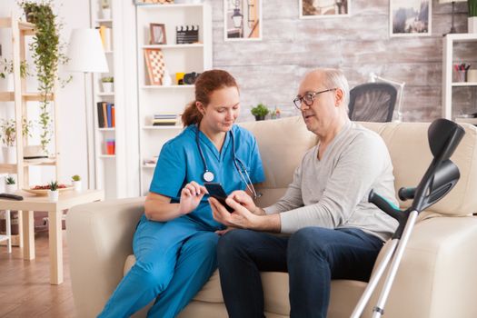 Female doctor in nursing home helping senior man to use his phone.