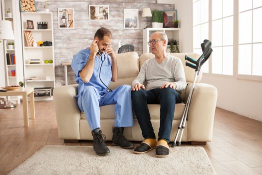 Male doctor with stethoscope in nursing home to check old man heart.