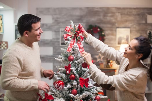 Young woman in matching clothes with her boyfriend putting the top ornament for christmas tree.