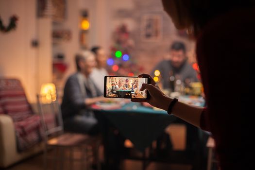 Granddaughter using her phone to take photos of the family at christmas celebration.