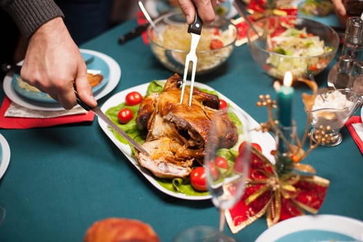 Delicious roasted chicken sliced by man at christmas celebration with his family.