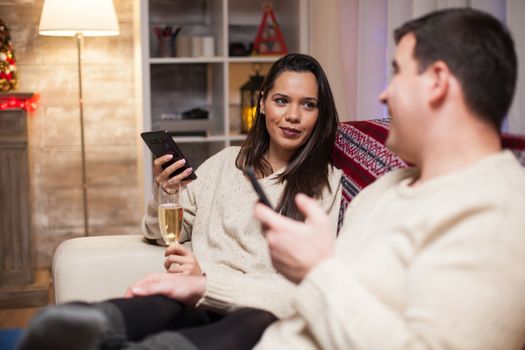 Young couple having a conversation holding their phones on christmas day. Woman a glass of champagne.