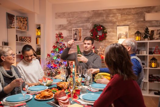 Happy father opening a bottle of wine at christmas family dinner. Delicious food.