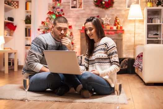 Happy couple in matching clothes doing online shopping for christmas on laptop.