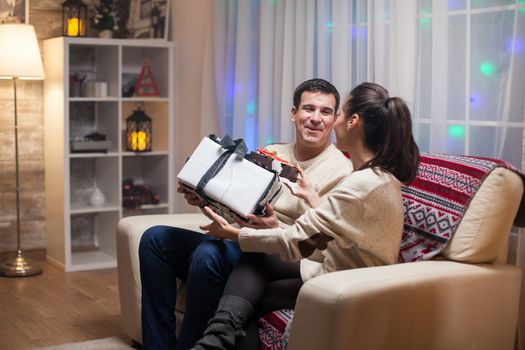 Young wife giving her husband a big present on christmas day. Happy couple.