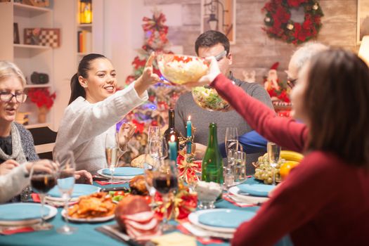 Happy woman passing the salad over the table to his daughter at christmas family dinner.