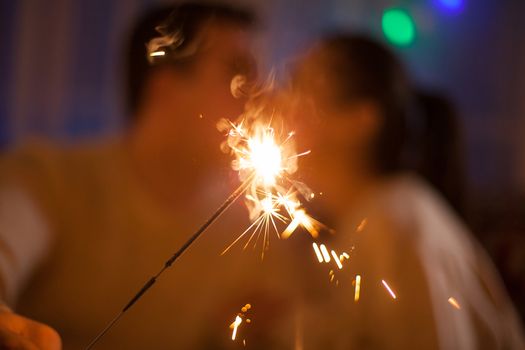 Young couple sitting on couch kissing and holding bengal lights on christmas day.