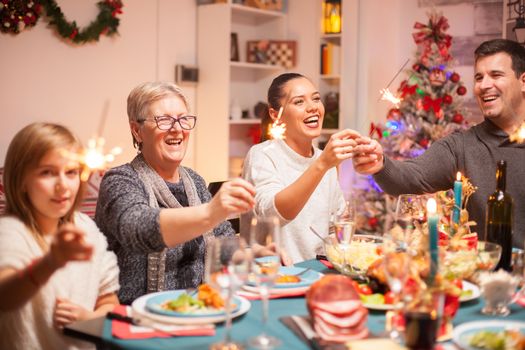 Senior woman and her daughter laughing at christmas celebration and holding hand fireworks.