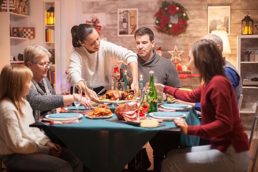 Cheerful woman arriving with tasty chicken from oven for her big family at christmas dinner.