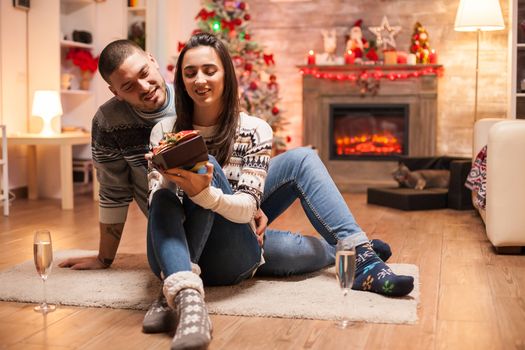 Happy girlfriend about her christmas gift from boyfriend in front of warm fireplace.