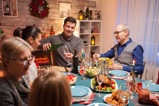 Husband pouring wine for his father in law at christmas celebration. Happy family