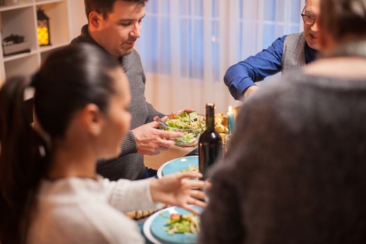 Cheerful man at christmas family dinner with a bowl with delicious salad.