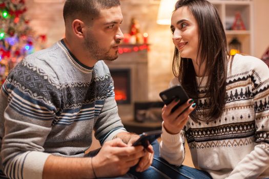 Happy couple looking into each other eyes on christmas. Browsing on phone.