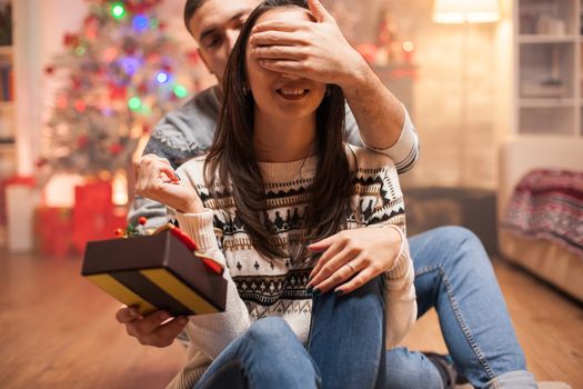 Happy boyfriend covering girlfriend's eyes while giving her christmas gift.