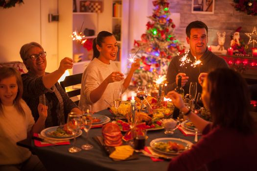 Big happy family singing at christmas celebration with delicious food and hand fireworks.