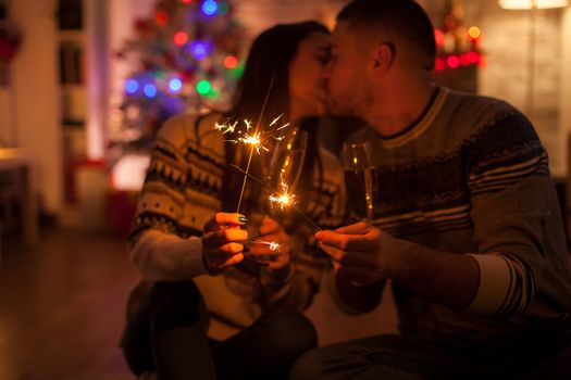 Couple kissing in dark room holding burning hand fireworks on christmas day.